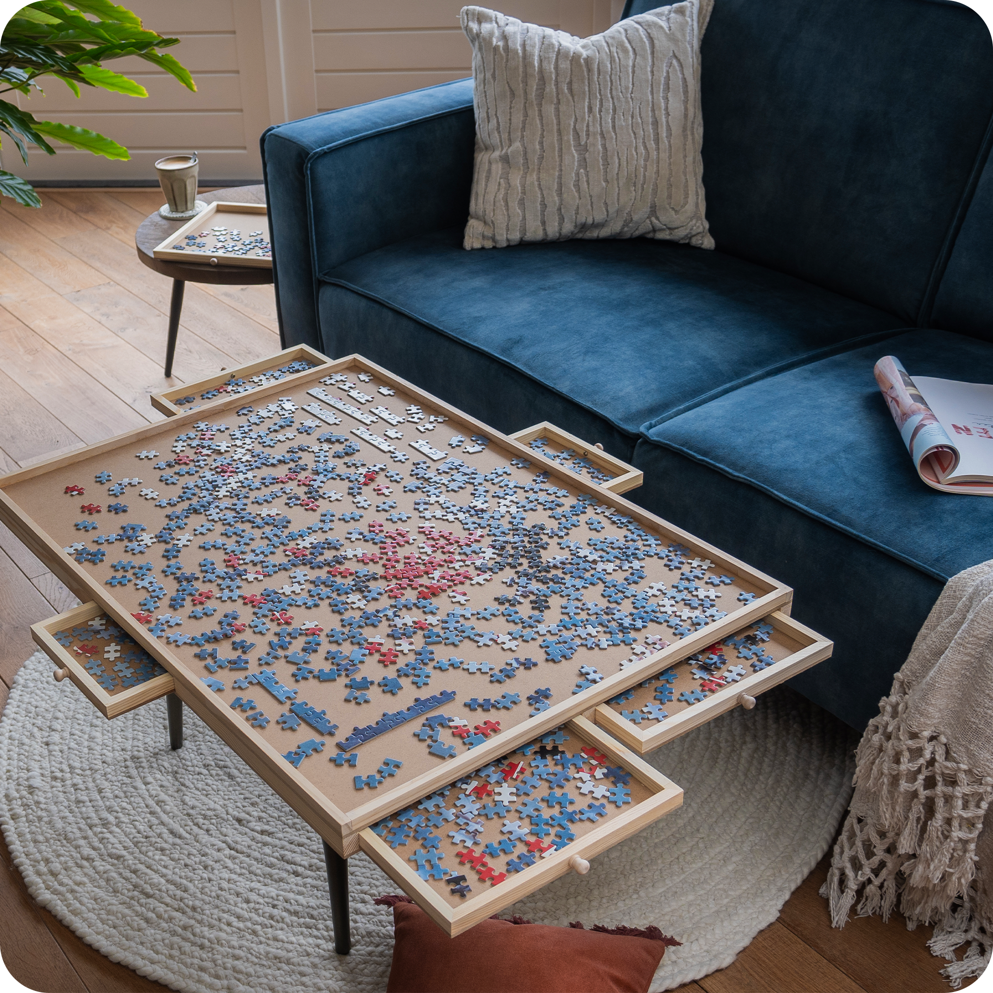 Een landelijke woonkamer met een blauwe bank en landelijke kussens en plaid. Op de salontafel staat een puzzelplaat waar een puzzel van 1000 stukjes wordt gemaakt.