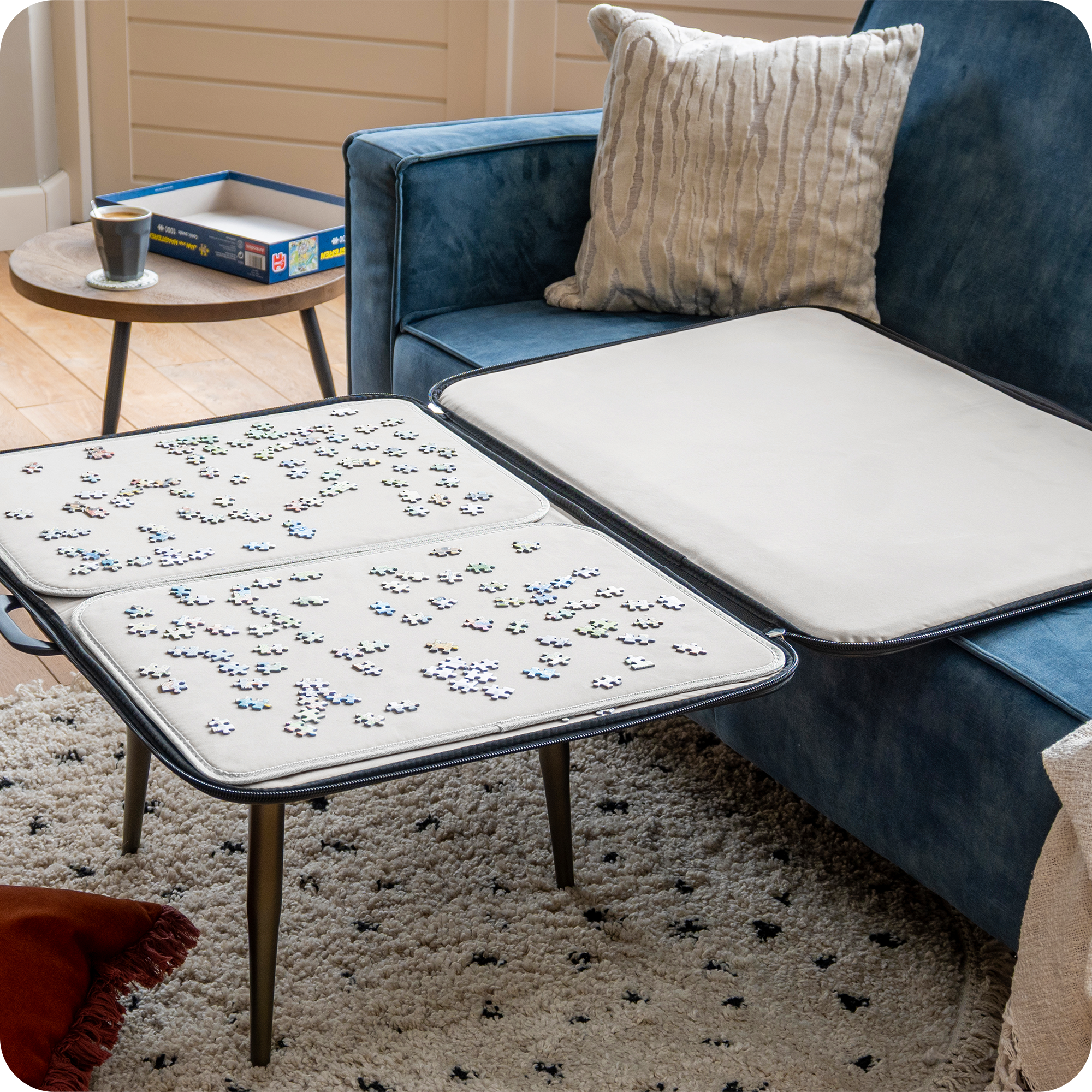Een moderne woonkamer met een blauwe bank en beige kussens. De puzzelmap ligt open op een salontafel waar een puzzel van 1000 stukjes op gemaakt wordt.